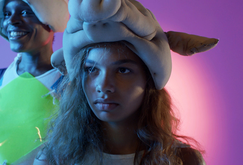 Madeline (Helena Howard) on stage, wearing a pig mask as a hat.