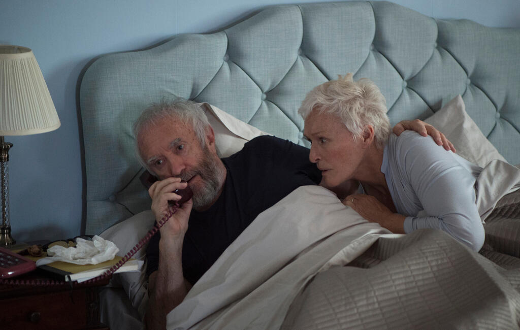 Joe (Jonathan Pryce) and Joan (Glenn Close) in bed. Joe is on the phone, Joan is anxiously listening to the call. 