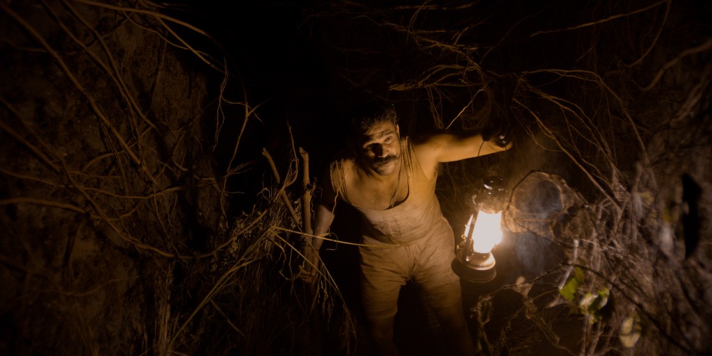Vinayak (Sohum Shah) in a hole, surrounded by roots.