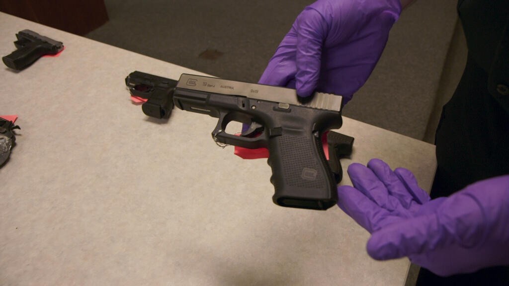 Two hands in violet plastic gloves showing off a handgun.