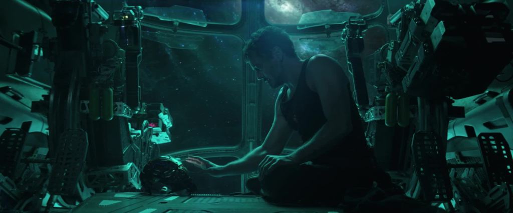 Tony Stark (Robert Downey Jr.) sitting in a spaceship, reaching for his Iron Man helmet.