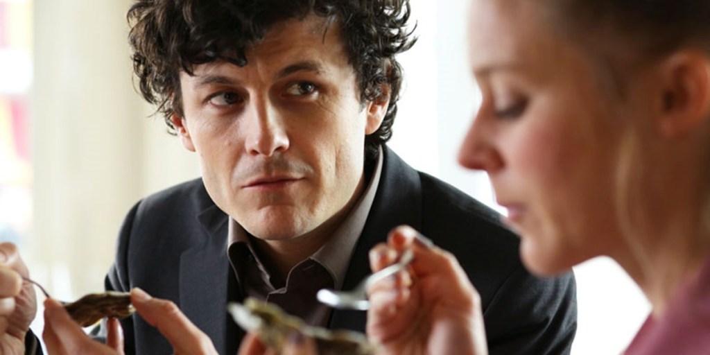 Gruber (Manuel Rubey) looking at Sarah (Bernadette Heerwagen) as they eat oysters.