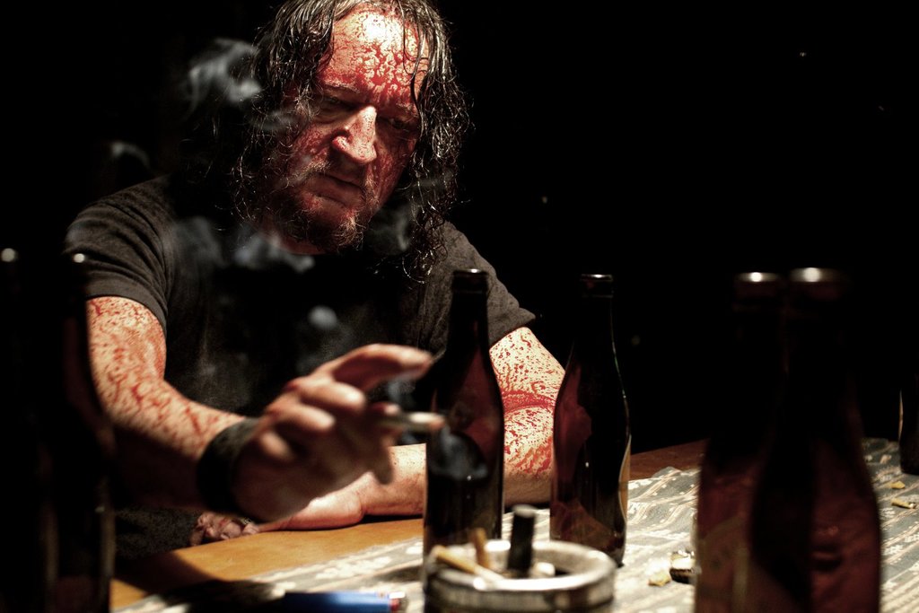 Karl (Andreas Sobik) sitting blood-spattered at a table.