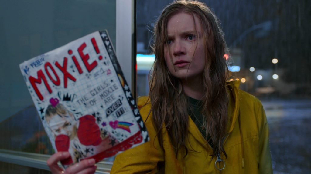 Vivian (Hadley Robinson) holding up a copy of the Moxie zine.