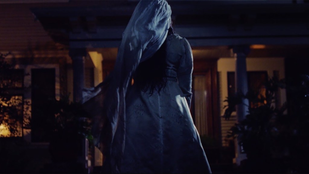 La llorona (Marisol Ramirez) dressed in a bridal gown, approaching a house in the dark.