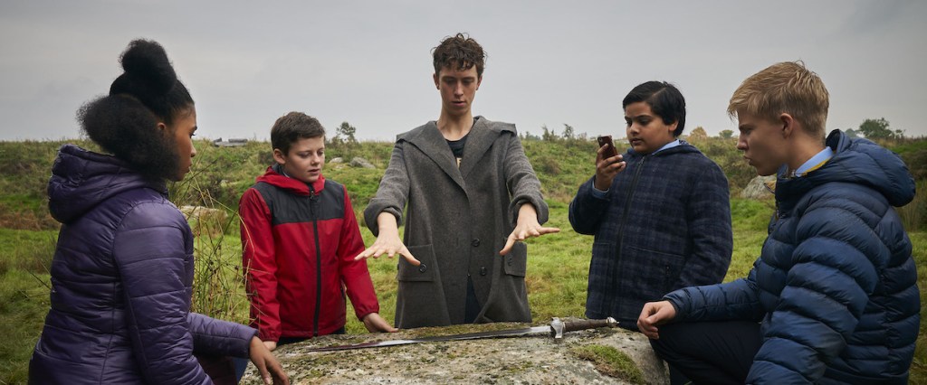 Merlin (Angus Imrie) holding his hands ovr a stone, surrounded by Kaye (Rhianna Dorris), Alex (Louis Ashbourne Serkis), Bedders (Dean Chaumoo) and Lance (Tom Taylor).