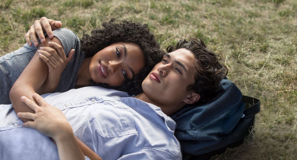 Natasha (Yara Shahidi) and Daniel (Charles Melton) cuddling in grass.