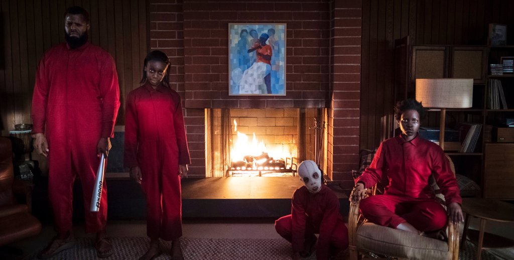 Abraham (Winston Duke), Umbrae (Shahadi Wright Joseph), Pluto (Evan Alex) and Red (Lupita Nyong'o), all wearing red overalls, standing and sitting in strange poses in the living room. 