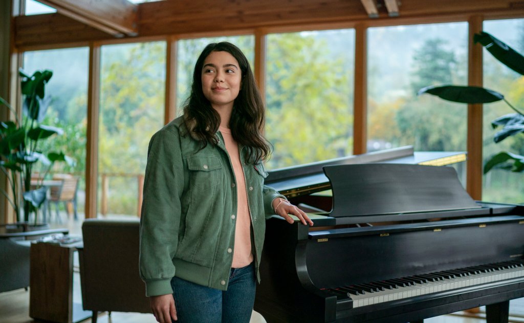 Amber (Auli'i Cravalho) standing next to a piano. 