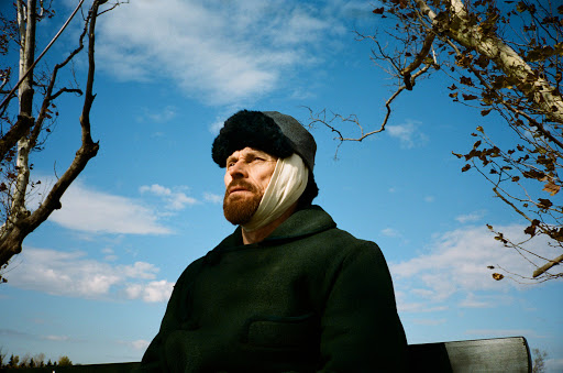 Vincent van Gogh (Willem Dafoe) with a bandaged ear sitting on a park bench. 