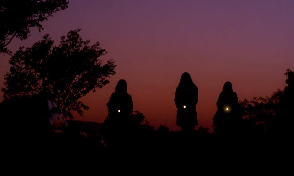 Three girls walking with flashlights. They can just be seen as silhouettes against the sunset. 