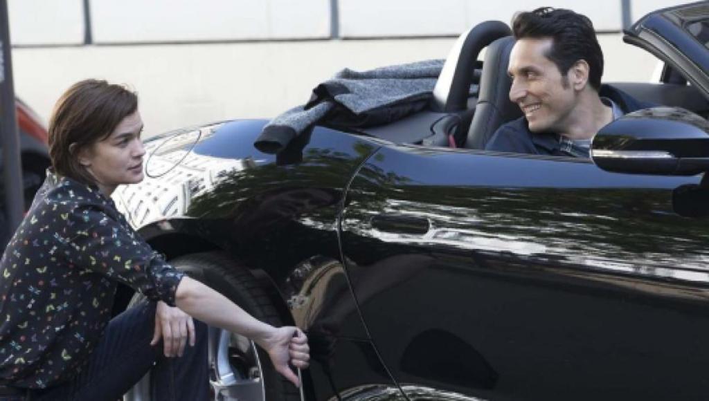 Damien (Vincent Elbaz) in the car with Alexandra (Marie-Sophie Ferdane) kneeling next to the car, fixing the tire.