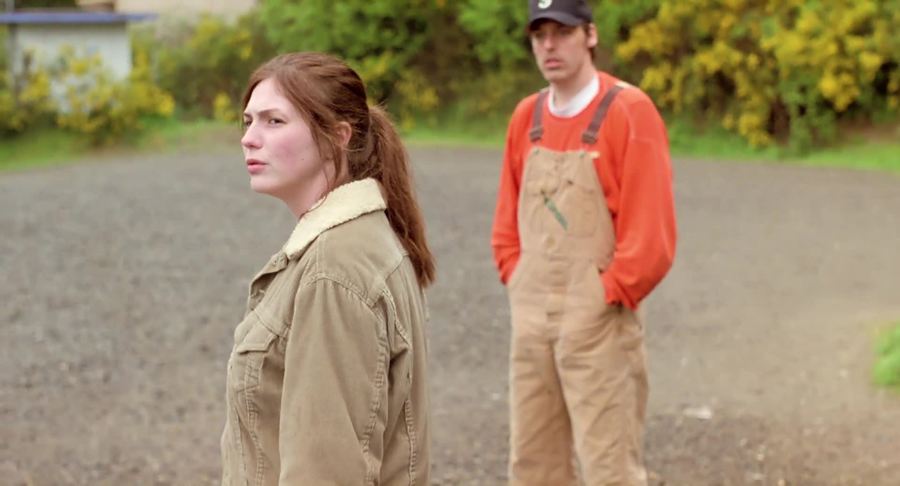 Kate (Amber Hubert) with a confused face, a guy standing behind her.