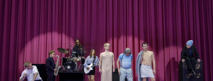 The cast, including a small band, standing in front of a huge pink curtain. 