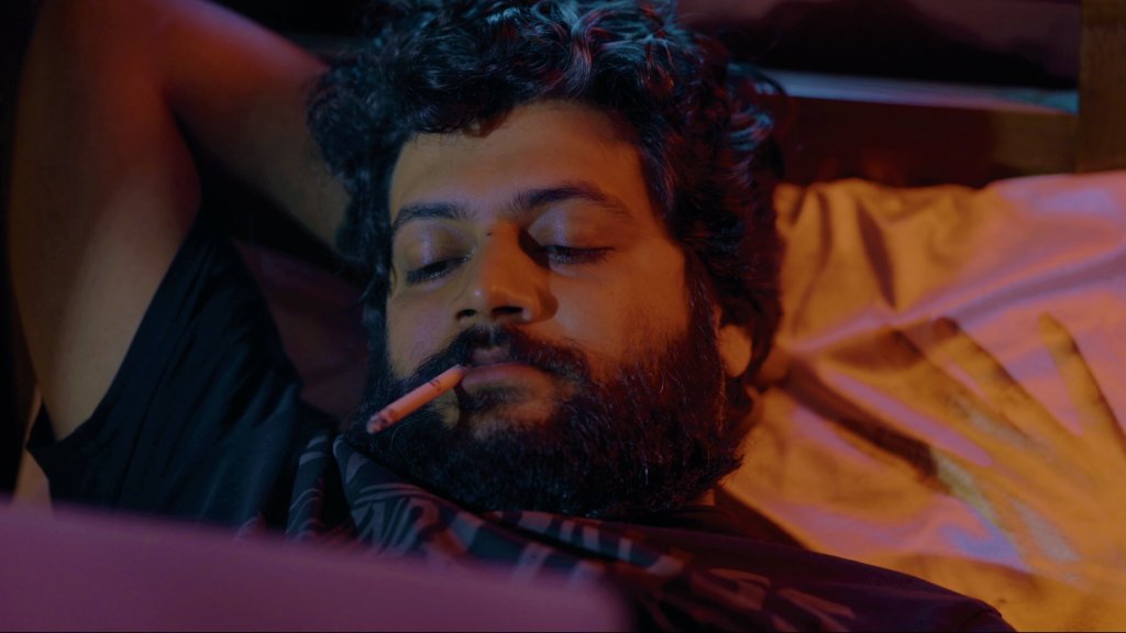 Vikrant (Vinay Sharma) lying on his bed, a cigarette in his mouth, a laptop balanced on his belly. 
