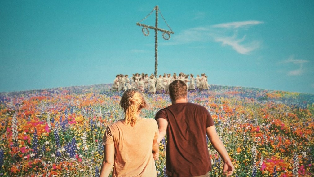 Christian (Jack Reynor) leading Dani (Florence Pugh) across a meadow full of flowers towards a group of people dancing around a huge wooden pole, all dressed in white.