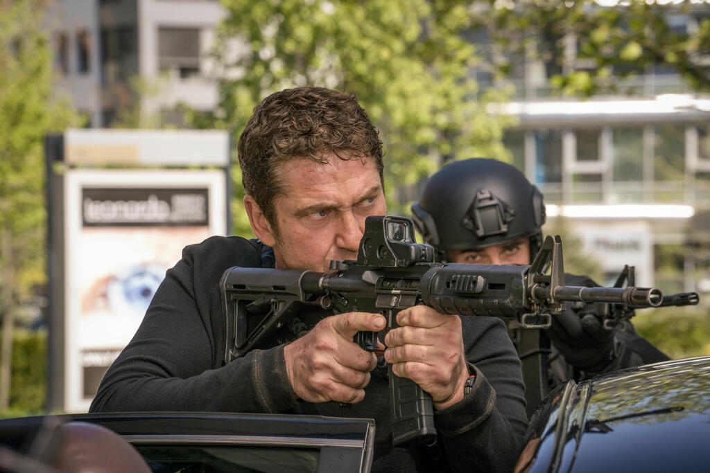 Mike Banning (Gerard Butler) aiming a machine gun over a car. 