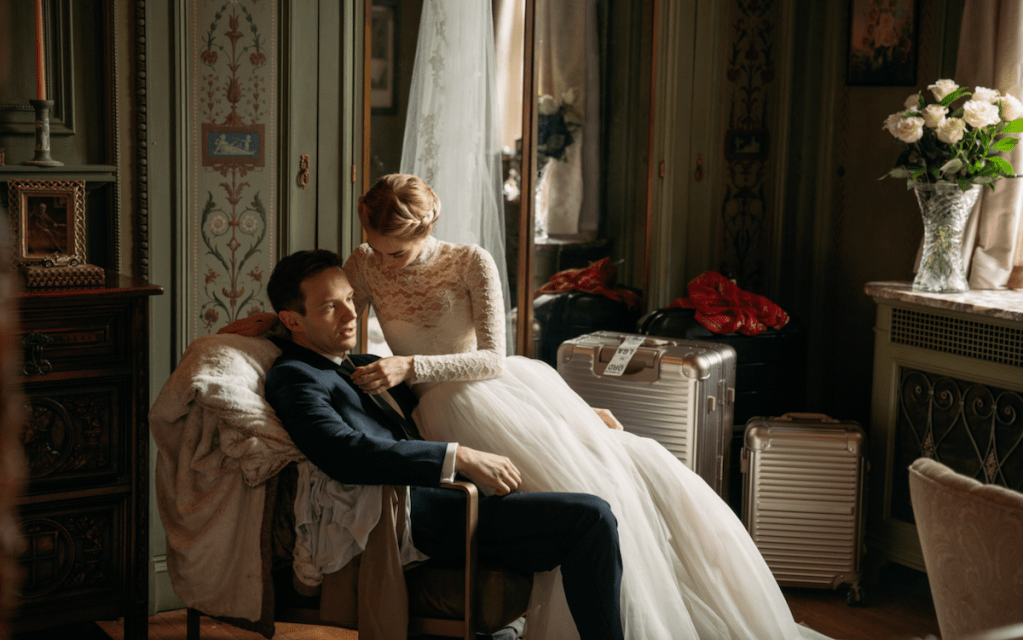Grace (Samara Weaving) wearing her wedding dress, sitting on the lap of her husband Alex (Mark O'Brien).