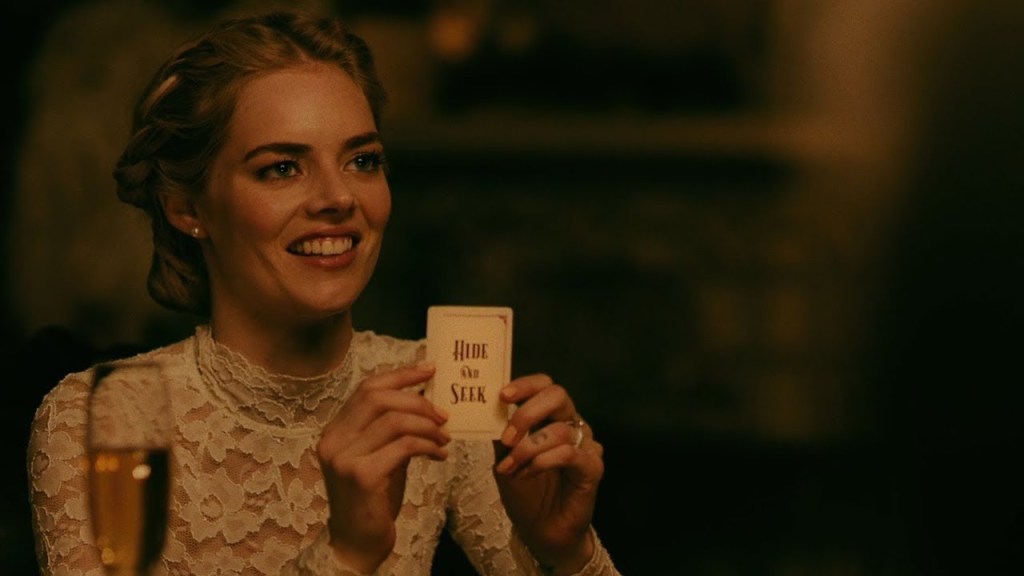 Grace (Samara Weaving) holding up a card that says "Hide and Seek".