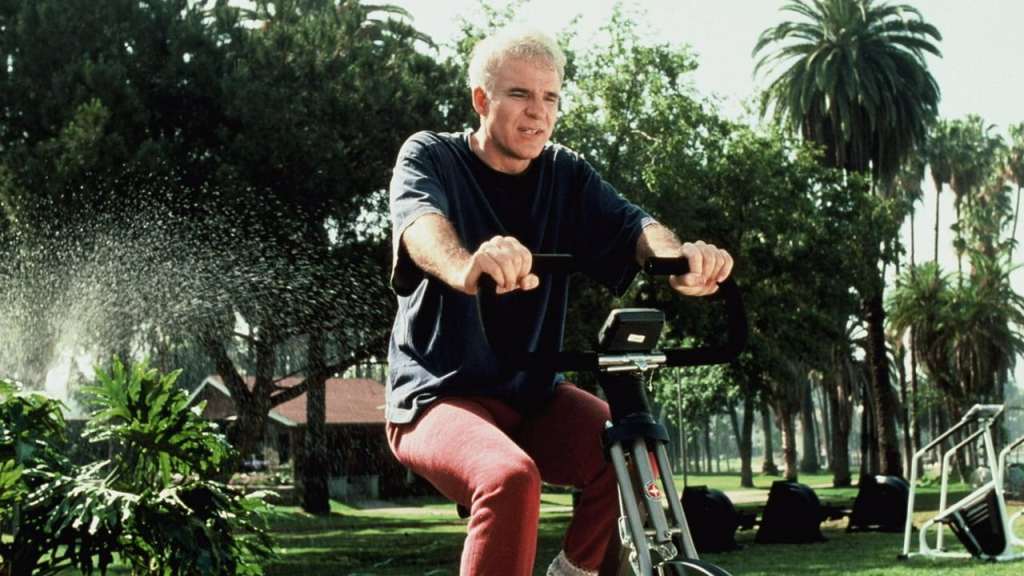 Harris (Steve Martin) on a hometrainer in a park.