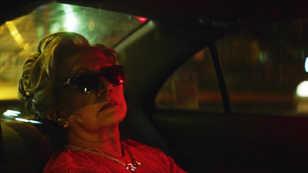 Nona (Josefina Ramírez) in the backseat of a car with her sunglasses on at night.