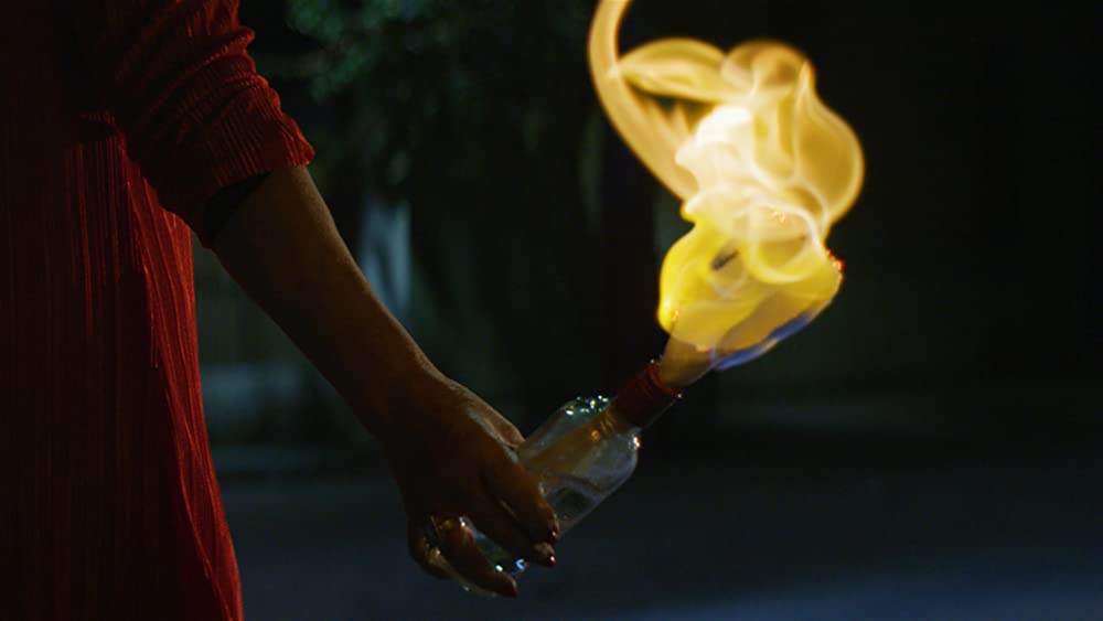 A hand holding a burning Molotov cocktail.