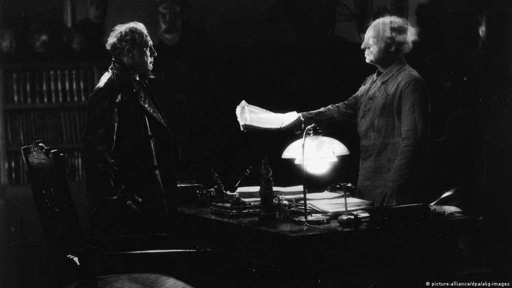 Translucent Mabuse (Rudolf Klein-Rogge) handing Prof. Baum (Oscar Beregi Sr.) papers.