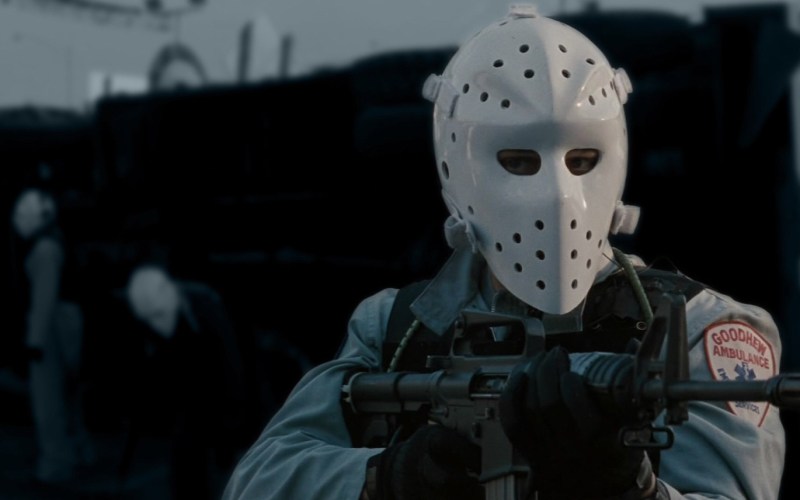 A masked man aiming an automated weapon.