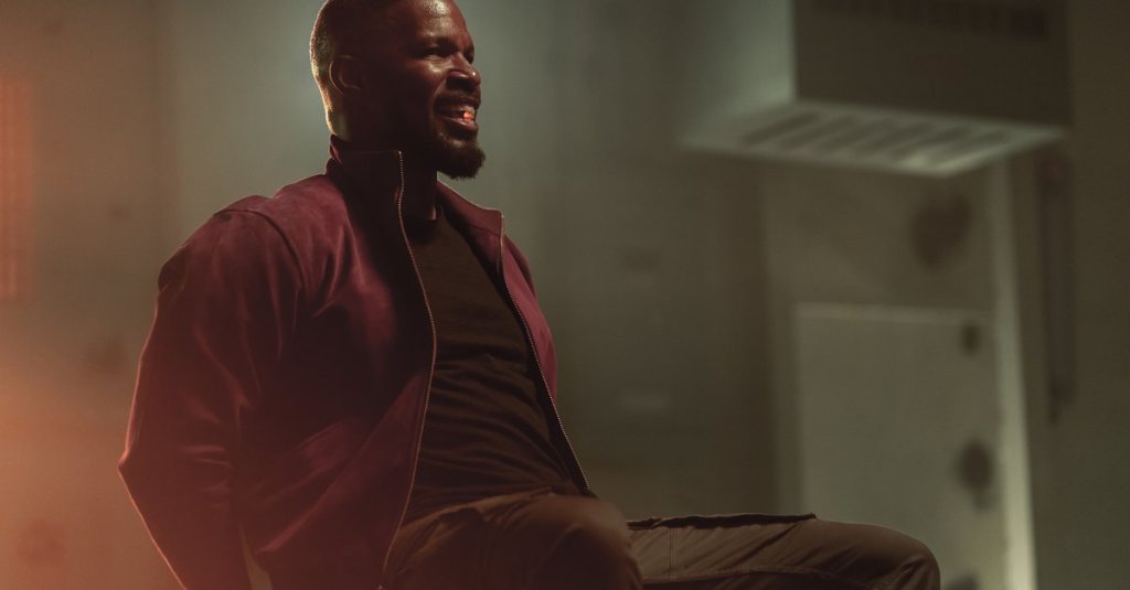 Art (Jamie Foxx) tied to a chair, a glowing pill between his teeth.