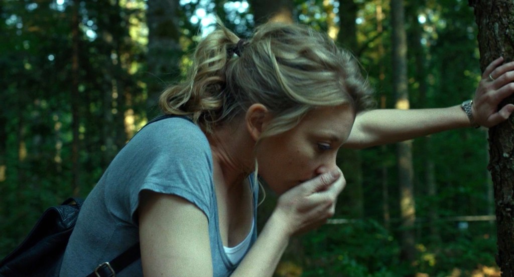 Sara (Natalie Dormer) leaning against a tree, one hand covering her face as if she's about to throw up.