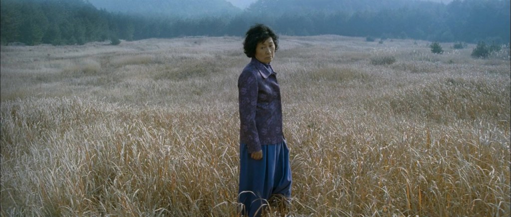 The mother (Hye-ja Kim) standing in wheat field.