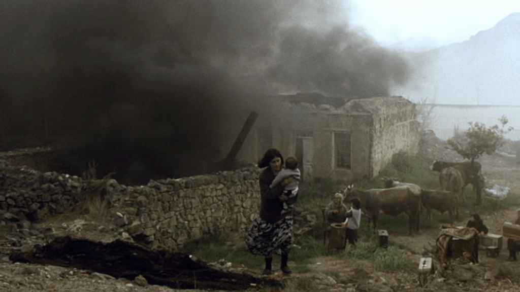 A woman carrying a baby away from a burning house. 