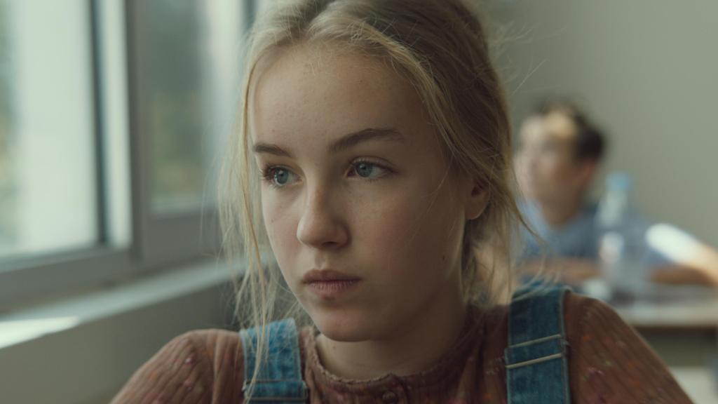 Mylia (Emilie Bierre) sitting in class, looking out the window.
