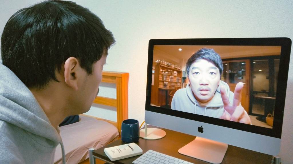 Kato (Kazunari Tosa) looking at himself on his computer screen. The screen version is holding up two fingers.