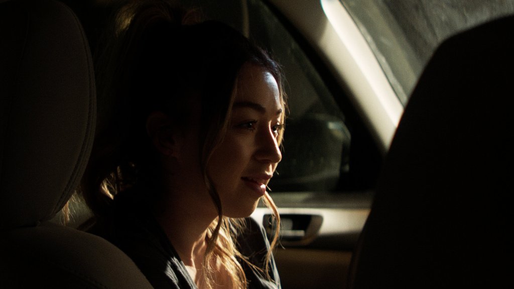 Kelsey (Shelby Duclos) sitting in the car, smilling.