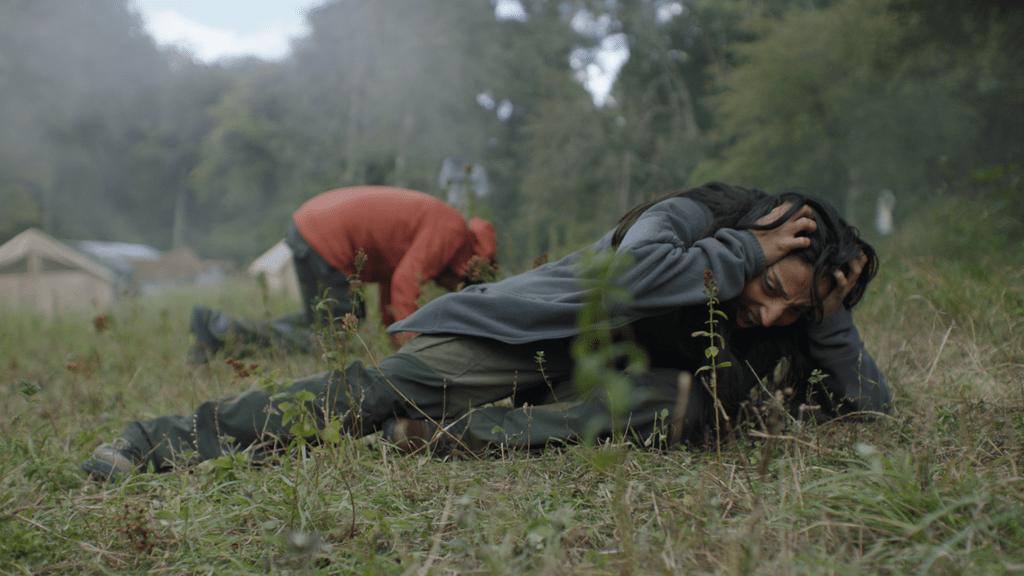 Alma (Ellora Torchia) and Martin (Joel Fry) lying on the forest floor, Alma clutching her head.