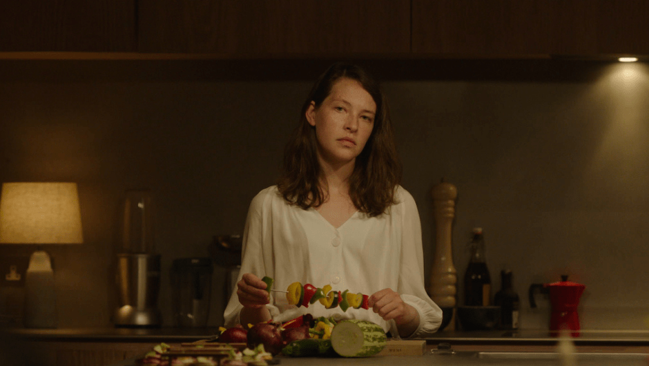 Cadi (Annes Elwy) pushing vegetables on a skewer with an absent-minded expression.