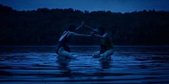 Miriam (Madeleine Sims-Fewer) and Greta (Anna Maguire) wrestling in the water while sitting on the shoulders of their husbands.