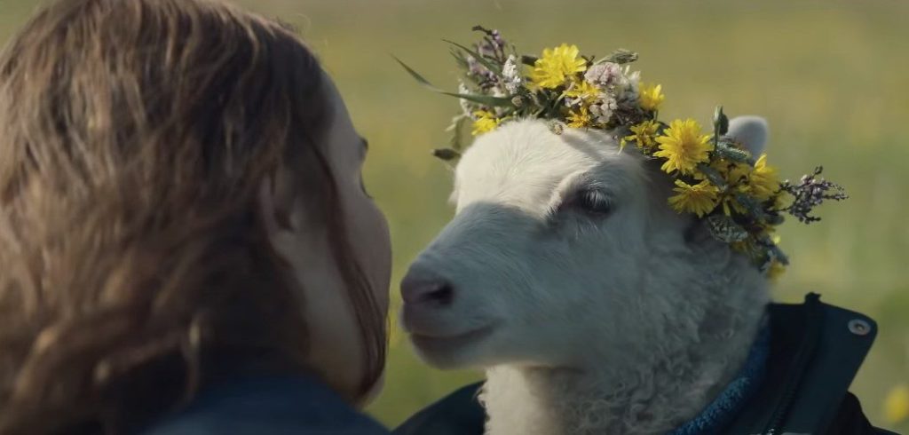 Maria (Noomi Rapace) cuddling with a lamb in a jacket that wears a flower crown.