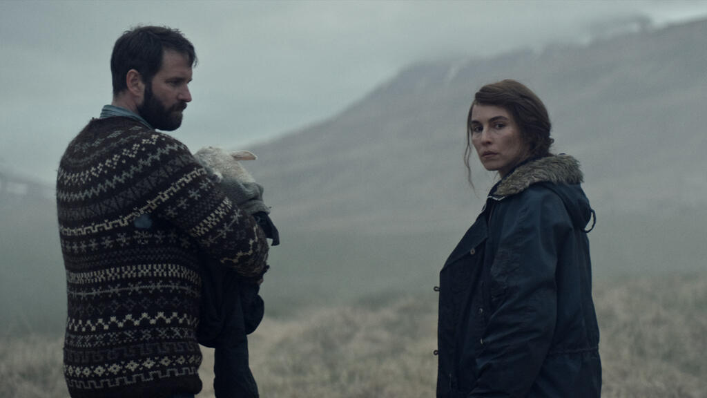 Ingvar (Hilmir Snær Guðnason) holding a lamb wrapped in a jacket in his arms. Maria (Noomi Rapace) is standing next to him, looking backwards.