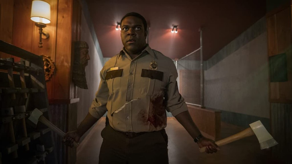 Finn (Sam Richardson) holding two axes, his uniform shirt bloodied and torn.
