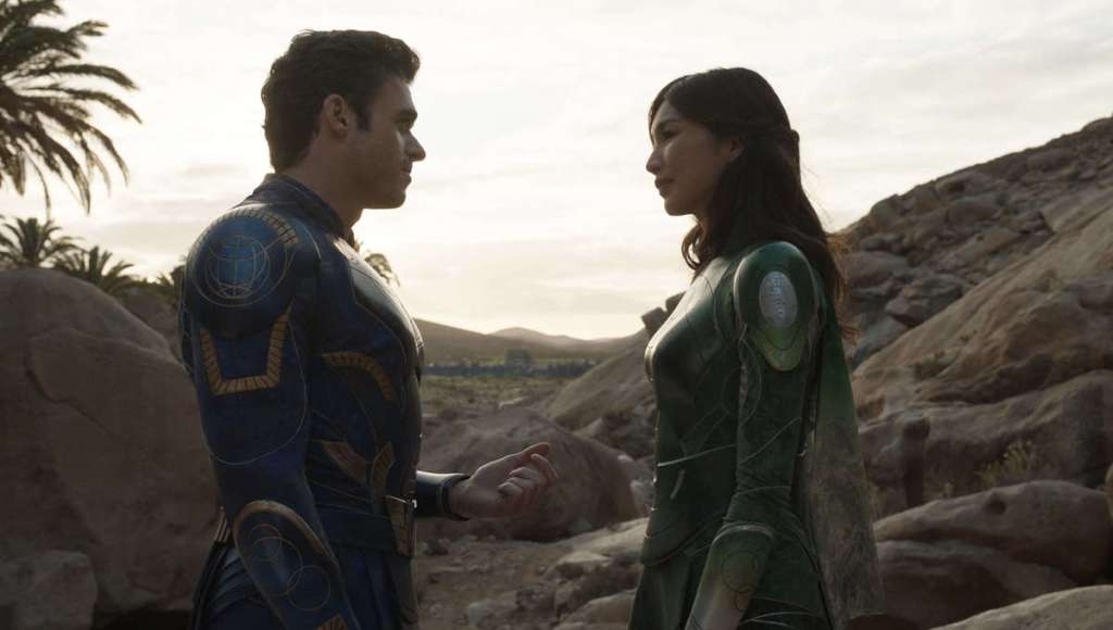 Ikaris (Richard Madden) and Sersi (Gemma Chan) in the desert. He is holding his hand out to her. 