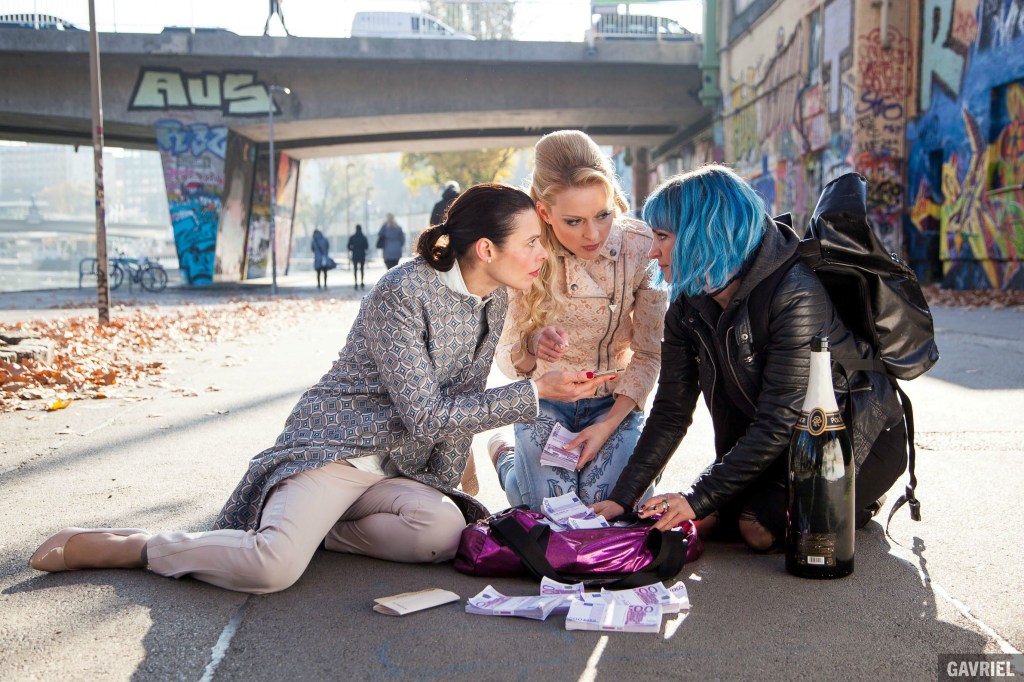 Nadja (Margarita Breitkreiz), Vera (Darya Nosik) and Teresa (Sabrina Reiter) huddling over a bag full of cash.