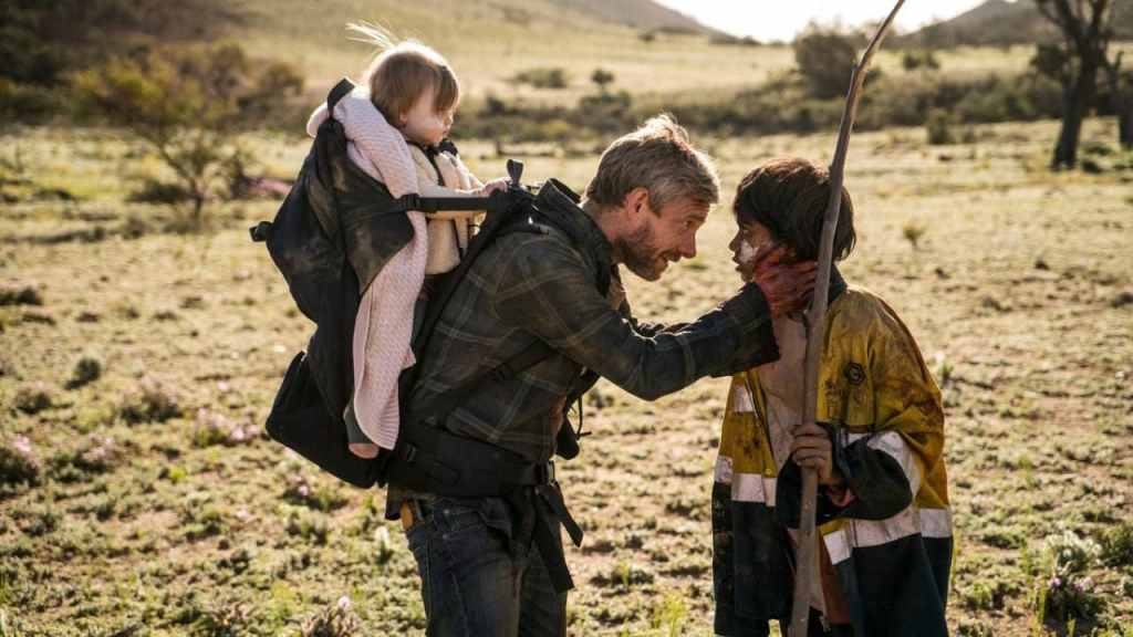 Andy (Martin Freeman) with his baby on his back, talking intently to Thoomi (Simone Landers).