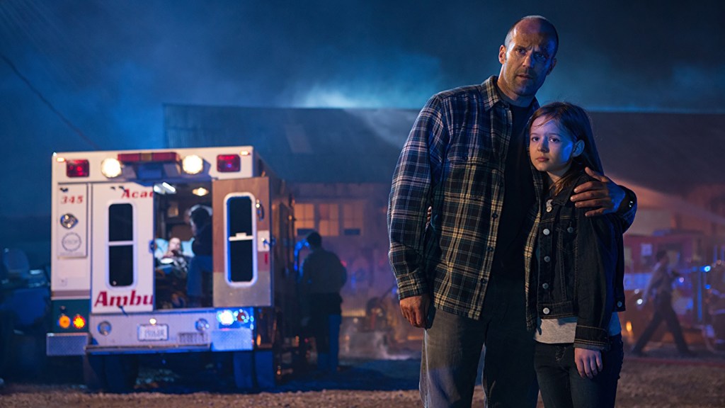 Phil Broker (Jason Statham) holding his daughter Maddy (Izabela Vidovic), behind them an ambulance and a burning house.