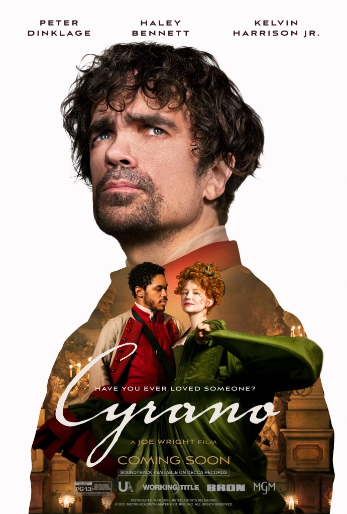 The film poster showing a big close-up of Cyrano (Peter Dinklage) looking into the distance, with Christian (Kelvin Harrison Jr. ) and Roxanne (Haley Bennett) holding each other in a smaller image beneath him.
