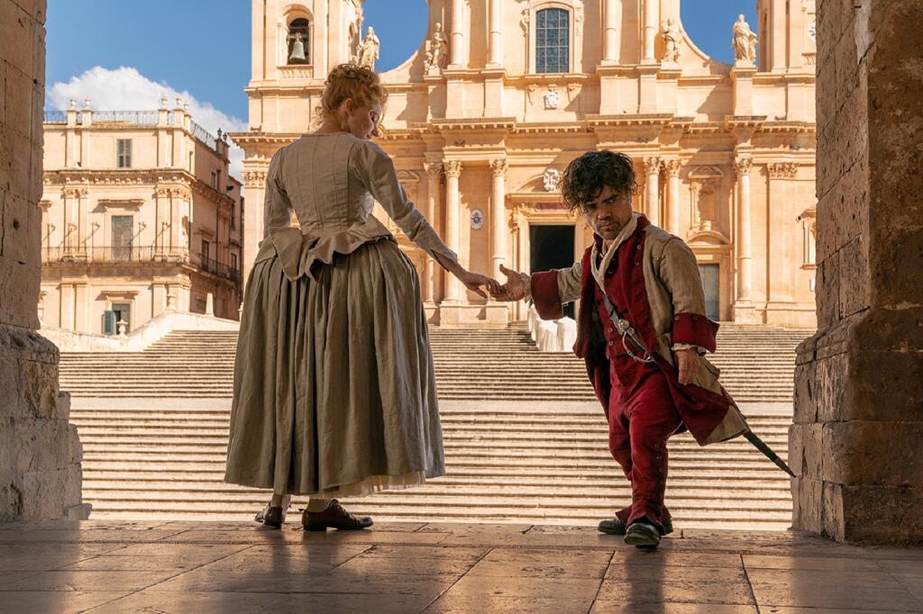 Roxanne (Haley Bennett) and Cyrano (Peter Dinklage) clasping hands as he turns away from her.