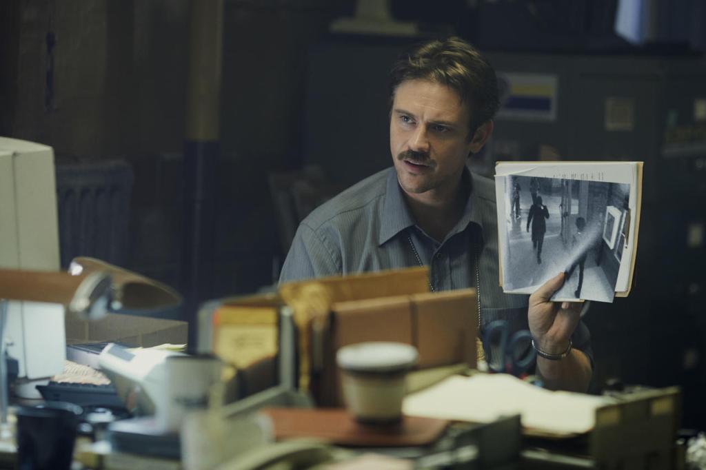 Locke (Boyd Holbrook) holding up a printout of surveillance footage that shows a hooded figure in a subway station.