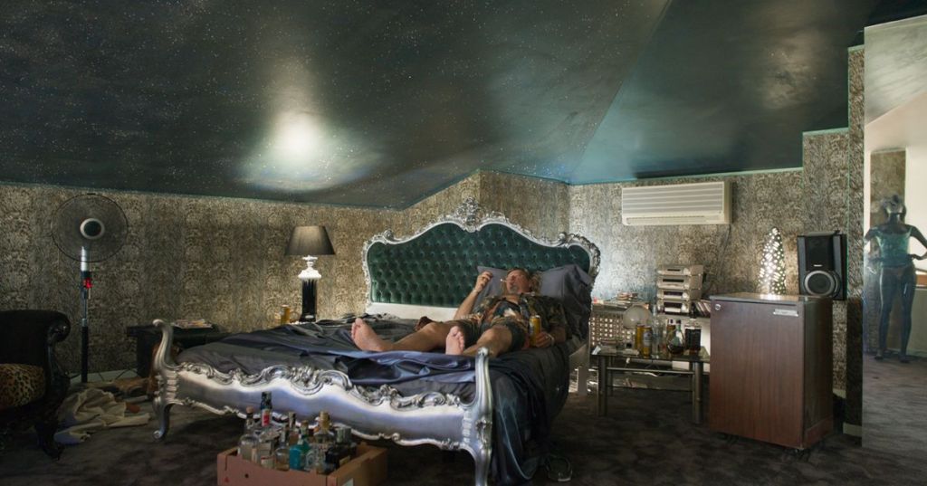 Richie Bravo (Michael Thomas) lying in his bed, drinking and smoking.