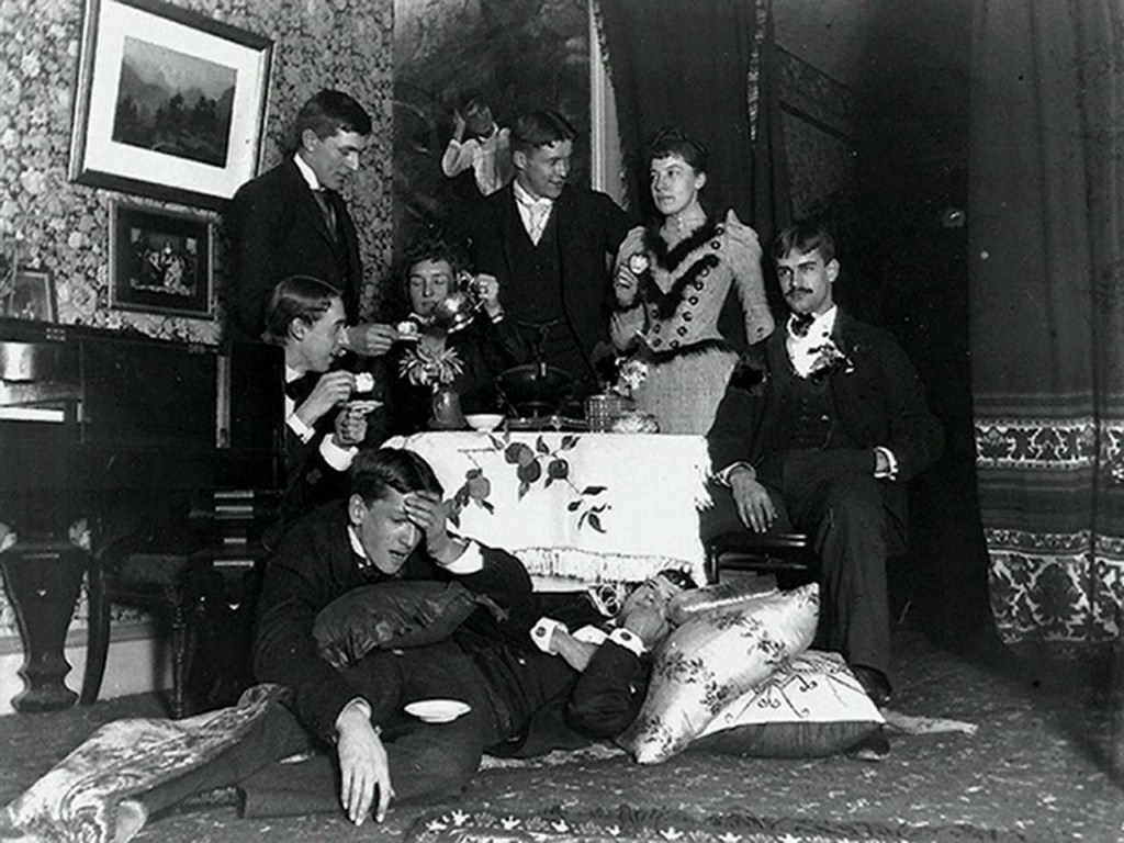 A photograph by Alice Austen showing herself and a group of friends in dramatic poses around a tea table.